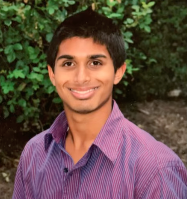 A young man with dark hair and a purple striped shirt smiles.